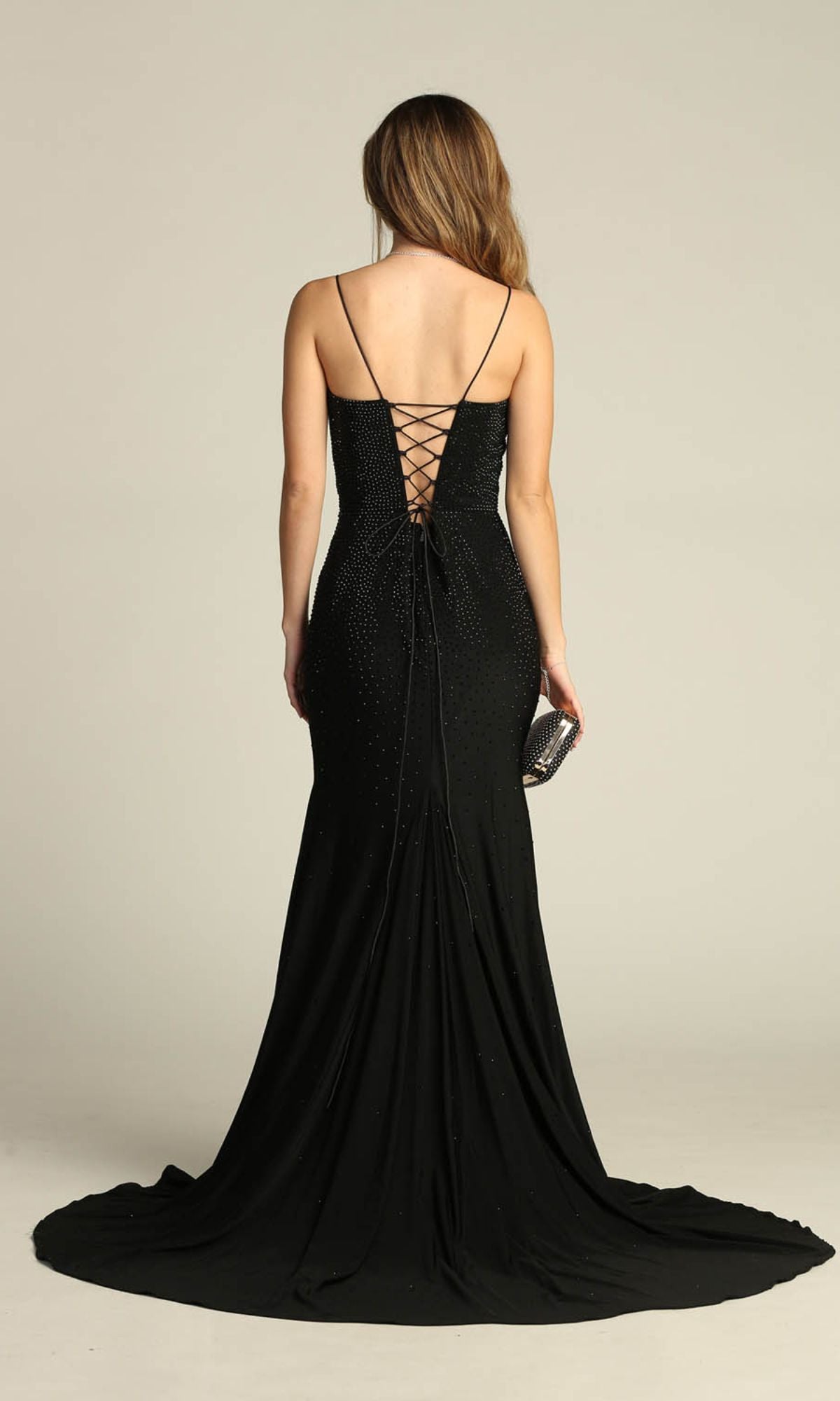 Woman in the Chicas YG5026 Lace-Up Long Beaded Prom Dress, black and backless with lace-up detail, holds a small clutch and stands facing away from the camera.